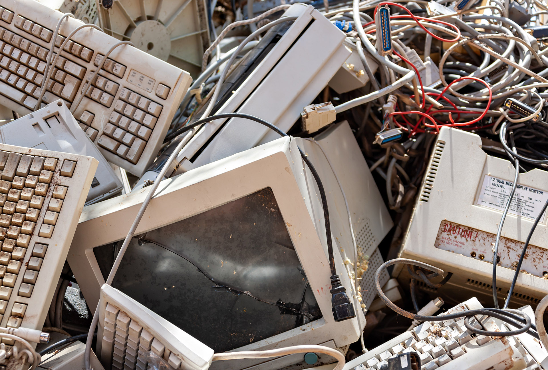 An old dilapitated computer discarded within a pile of other broken electronics